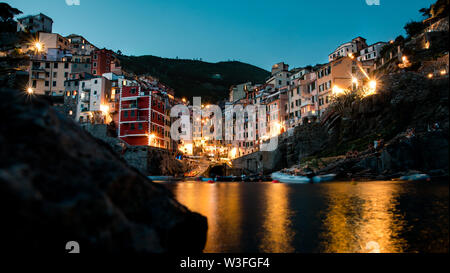 Eine der fünf Länder Städte Riomaggiore von einem niedrigen Winkel am Wasser als lange Belichtung bei Nacht fotografiert. Stockfoto