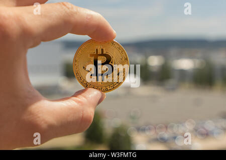 Man Finger halten einen großen runden Golden bitcoin Münze vor der industriellen Stadt. Stockfoto