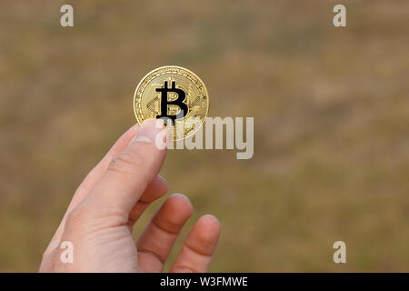 Man Finger halten einen großen runden Golden bitcoin Münze vor gelb grün Muster. Stockfoto