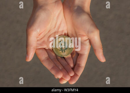 Blick von oben auf die weibliche Hände halten viele Münzen von Bitcoin auf dem Hintergrund der grauen Asphalt in den Strahlen der Sonne. Stockfoto