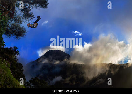 Ein Mädchen auf Schaukel am Ende der Welt gegen die Ansicht der Vulkan Tungurahua in wunderschönen Sonnenuntergang Explosion Stockfoto