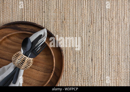 Ort, Einstellung auf Glasgewebe Hintergrund mit zwei gestapelten Holzplatten und Bettwäsche Serviette mit Black Metal Bestecke und Korbwaren Serviettenring Stockfoto