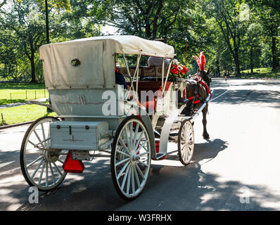 Eine rot-weiße Kutsche ertrinken nimmt Touristen auf einem Rundgang durch den Central Park an einem schönen Sommermorgen. Stockfoto