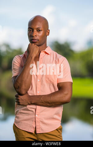 Portrait von Happy reife afrikanische amerikanische Mann im rosa Button Sommer Shirt und Kamera outdoor. Mann mit der Hand unter das Kinn Gefühl konfi Stockfoto