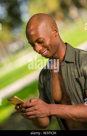 Porträt von einem gutaussehenden jungen afrikanischen amerikanischen Mann lächelnd und Senden einer SMS-Nachricht auf sein Smartphone Stockfoto