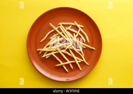 Rohe pasta strozzapreti in einem braunen Teller über einen gelben Hintergrund Stockfoto