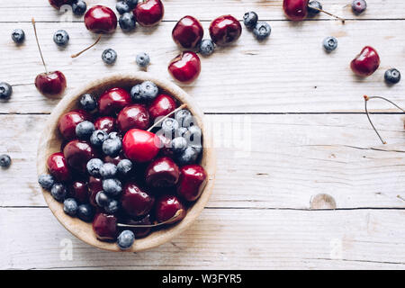 Schüssel von reifen Kirschen und Heidelbeeren. Große Sammlung von frisch gepflückte reife Beeren auf Holz- Hintergrund. Kopieren Sie Platz. Stockfoto