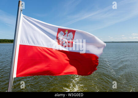 Polnische Flagge am Heck eines kleinen Binnen schiff ausgesetzt. Ein Schiff schwimmt auf einem großen See in Mitteleuropa. Jahreszeit des Sommers. Stockfoto