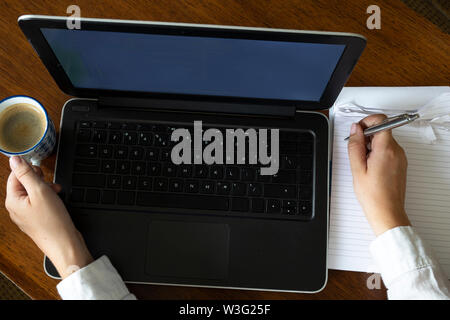 Blick von oben auf die Weibchen mit Ihrem Laptop auf einen hölzernen Tisch. Overhead shot der jungen Frau, die an einem Tisch sitzen mit einer Tasse Kaffee Stockfoto