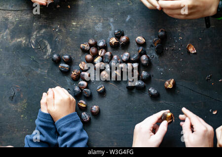 Hände, die gebratenen Kastanien auf einem Holztisch mit auch Kastanie Igel Stockfoto