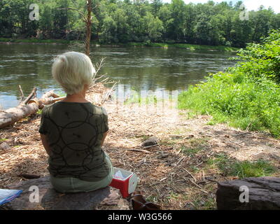 Dame auf einem Felsen mit einem Mittagessen kühler, genießen den Delaware River entlang der Route 97 im Staat New York. Auf der anderen Seite des Flusses liegt, Pennsylvania. Stockfoto