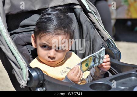 3 oder 4 Jahre alten Kind spielen mit gefälschten Papier Geld Hundert-Euro-Scheine in Kinderwagen runzelte die Stirn und echte Menschen zu fairen Stockfoto