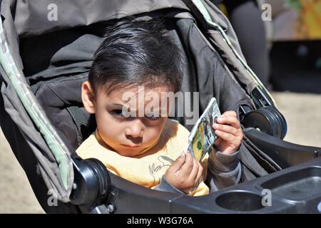 3 oder 4 Jahre alten Kind spielen mit gefälschten Papier Geld Hundert-Euro-Scheine in Kinderwagen runzelte die Stirn und echte Menschen zu fairen Stockfoto