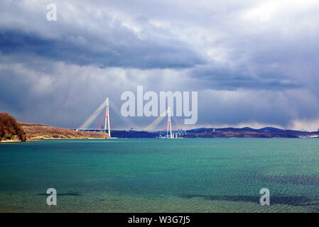 Bucht am Meer mit türkisfarbenem Wasser. Im Hintergrund Schrägseilbrücke. Stürmischen Himmel bedeckt. Russland, Wladiwostok, Insel Russisch Stockfoto