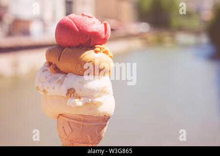 Nahaufnahme Bild der Frau Hand frische Waffel Kegel mit Vanille und Himbeere Eis auf der Holz- Hintergrund. Wandern. Im Freien Stockfoto