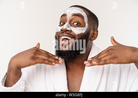 Junge afrikanische amerikanische Kerl Anwendung Gesicht Creme auf weißem Hintergrund. Portrait einer jungen Glücklich lächelnde afrikanischer Mann im Studio. High Fashion männliches Modell. Stockfoto