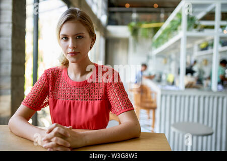 Lifestyle Portrait von selbstbewussten jungen trendigen tausendjährigen Geschäftsfrau mit blonden Haaren sitzen an den hölzernen Tisch in hellen und modernen Restaurant Stockfoto