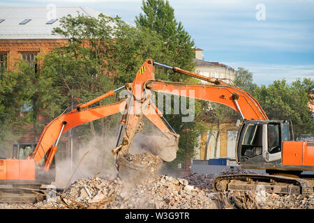 Zwei orangefarbene Bagger arbeiten auf den Trümmern eines zerstörten Gebäudes. Reinigung der Schutt, Gebäudeabbruch und Clearing Website Thema Bild Stockfoto