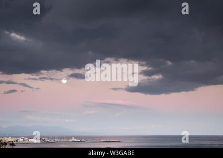 Sonnenuntergang am Strand von belameda in Spanien in Richtung Hafen mit einem vollen Mond im Himmel suchen Stockfoto