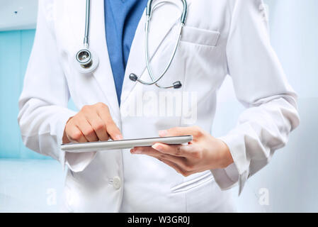 Frau Doktor im weißen Kittel und Stethoskop mit Tablette am Krankenhaus Stockfoto