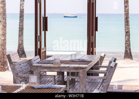 Tropical Beach Cafe mit Holztisch und Stühlen mit Blue sea water auf Hintergrund, Thailand. Rustikale Holzmöbel auf einen Balkon mit Blick auf einen beaut Stockfoto