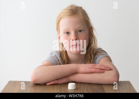 Ein junges Mädchen schaut auf eine einzige Marshmallow, Versuch, der Marshmallow test Stockfoto