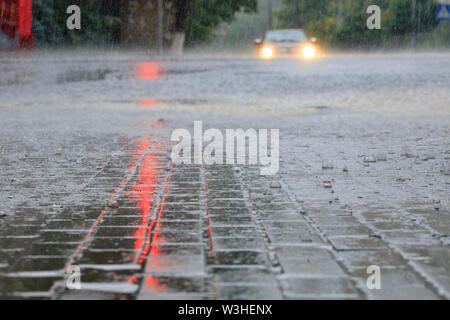 Die sintflutartigen Regenfälle an einer leeren Kreuzung und rotes Licht in der Strömung von Wasser auf einer Straße der Stadt wider. Stockfoto