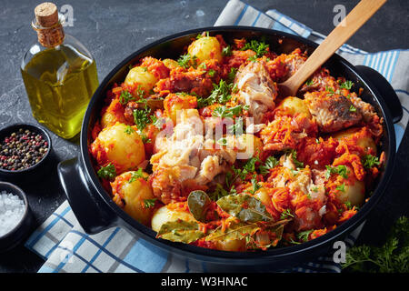 In der Nähe von geschmortem Seehecht gekocht mit neuen Kartoffeln und Gemüse in einen schwarzen keramischen Pfanne, Ansicht von oben Stockfoto