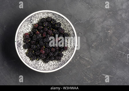 Frische rohe Maulbeeren in der Platte auf dunklen konkreten Hintergrund. Ansicht von oben mit der Kopie. Flach Hintergrund Stockfoto