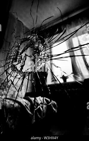 Zerbrochenes Glas mit Rissen und ein Loch stilisierten Schwarzweiß-Film und Lomography im Hintergrund der Fenster im Zimmer Stockfoto