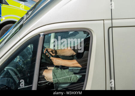 London, Großbritannien. 15. Juli 2019. Ein Fahrer verwendet sein Handy während der Fahrt über die Waterloo Bridge, trotz der Fahrt vorbei an der Polizeieskorte zum Aussterben Rebellion März. Credit: Guy Bell/Alamy leben Nachrichten Stockfoto