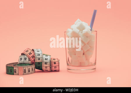 Glas voller Würfel Zucker mit Stroh auf einer schönen Pfirsich Hintergrund - ungesunde Ernährung Konzept. Stockfoto