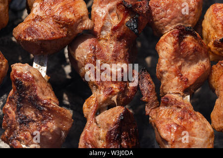 Kochen im Sommer Picknick - appetitlich saftiges Schweinefleisch shish Kebabs auf Metall Spieße auf Holzkohle Grill mit duftenden Feuer Rauch. Nahaufnahme, selectiv Stockfoto