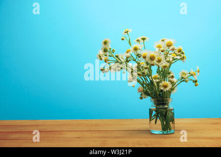 Schöne Kamille in Vase auf einem roten Holztisch und blauem Hintergrund behid. Stockfoto