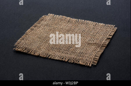 Alte sackleinen Stoff serviette Nahaufnahme. Grobes Leinen, Jute sack Stück auf schwarzem Hintergrund isoliert. Hessische Textur Tuch tag mit ausgefransten Rändern. Dark sa Stockfoto