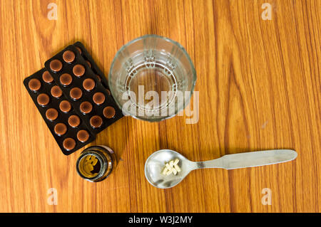 Blick von oben auf die Medizin Pillen oder Tabletten in Löffel, Flaschen und ein Glas Wasser mit einer Blisterpackung auf hölzernen Tisch Hintergrund. Apotheke Heilung und h Stockfoto