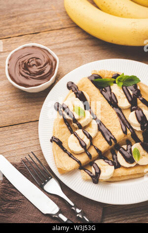 Crepe mit Bananen und Schokolade auf weiße Platte auf Holztisch mit Schokolade haselnuss Verbreitung serviert, Ansicht von oben Stockfoto