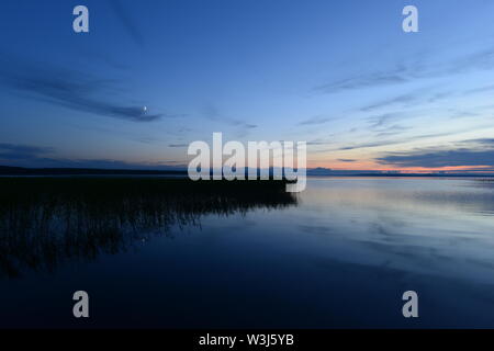 Mondaufgang im blauen Himmel vor Einbruch der Dunkelheit die in der Stille der See Wasser Stockfoto