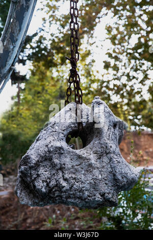 Eine große Granit Stein mit einem Loch hängt an einer rostigen eisernen Kette. Stein Gegengewicht zu den gut auf die Kette um eine Festung zu bauen. Anchor Last Stockfoto