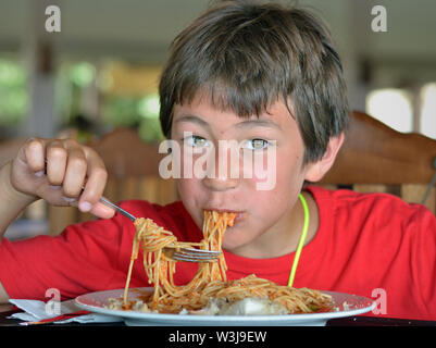 Süße kleine kanadische Junge von Mixed-race Ursprungs (Kaukasische und Südostasiatischen) Grabungen in einen Teller Spaghetti. Stockfoto