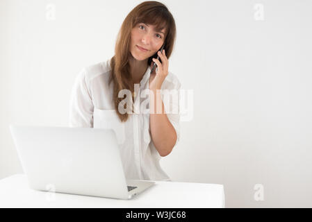 Young Professional freundliche Frau Gespräch am Handy mit Laptop im Büro Stockfoto