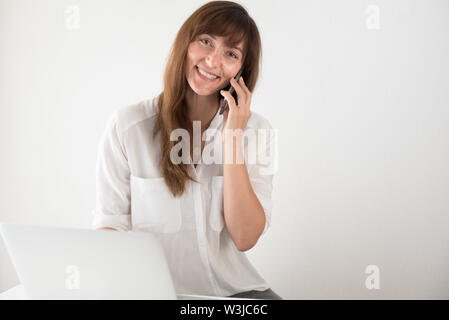 Young Professional freundliche Frau Gespräch am Handy mit Laptop im Büro Stockfoto