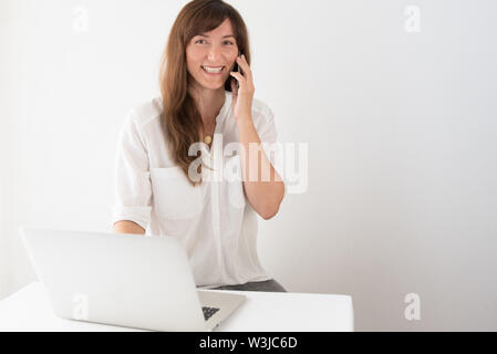 Young Professional freundliche Frau Gespräch am Handy mit Laptop im Büro Stockfoto