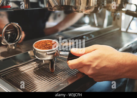 Barista holding Kaffee mit gemahlenem Kaffee in der Nähe von professionelle Kaffeemaschine bereitet Espresso im Cafe in der Nähe Stockfoto