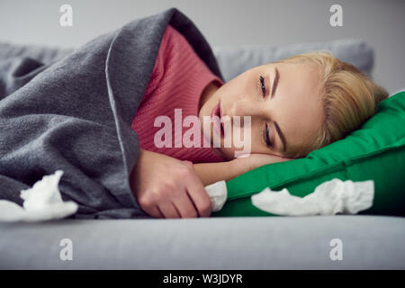 Frau leidet Kälte, Virus lag auf dem Sofa unter der Decke Stockfoto