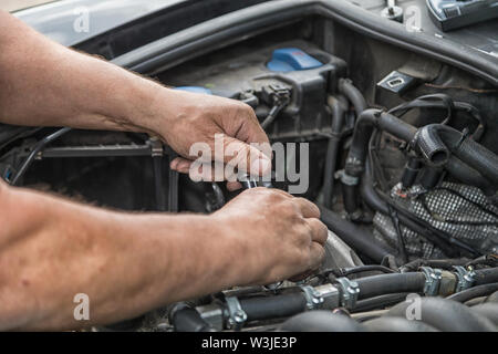 Zwei Hände Reparaturen im Motorraum eines Autos. Stockfoto