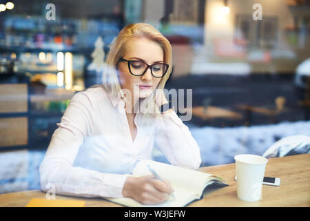 Nachdenkliche junge Frau sich Notizen während der Kaffeepause im Cafe Stockfoto