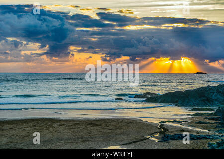 Sonnenstrahlen durch die Wolken bei Sonnenuntergang am Strand von Cornwall brechen Stockfoto