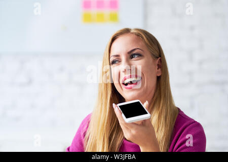 Glückliche Frau sprechen über das Telefon im Büro mit Smartphone Lautsprecher im Büro Stockfoto