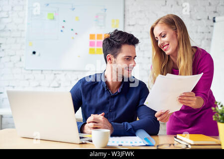 Attraktive junge geschäftsfrau über Dokumente und Flirten mit Kollegen Stockfoto